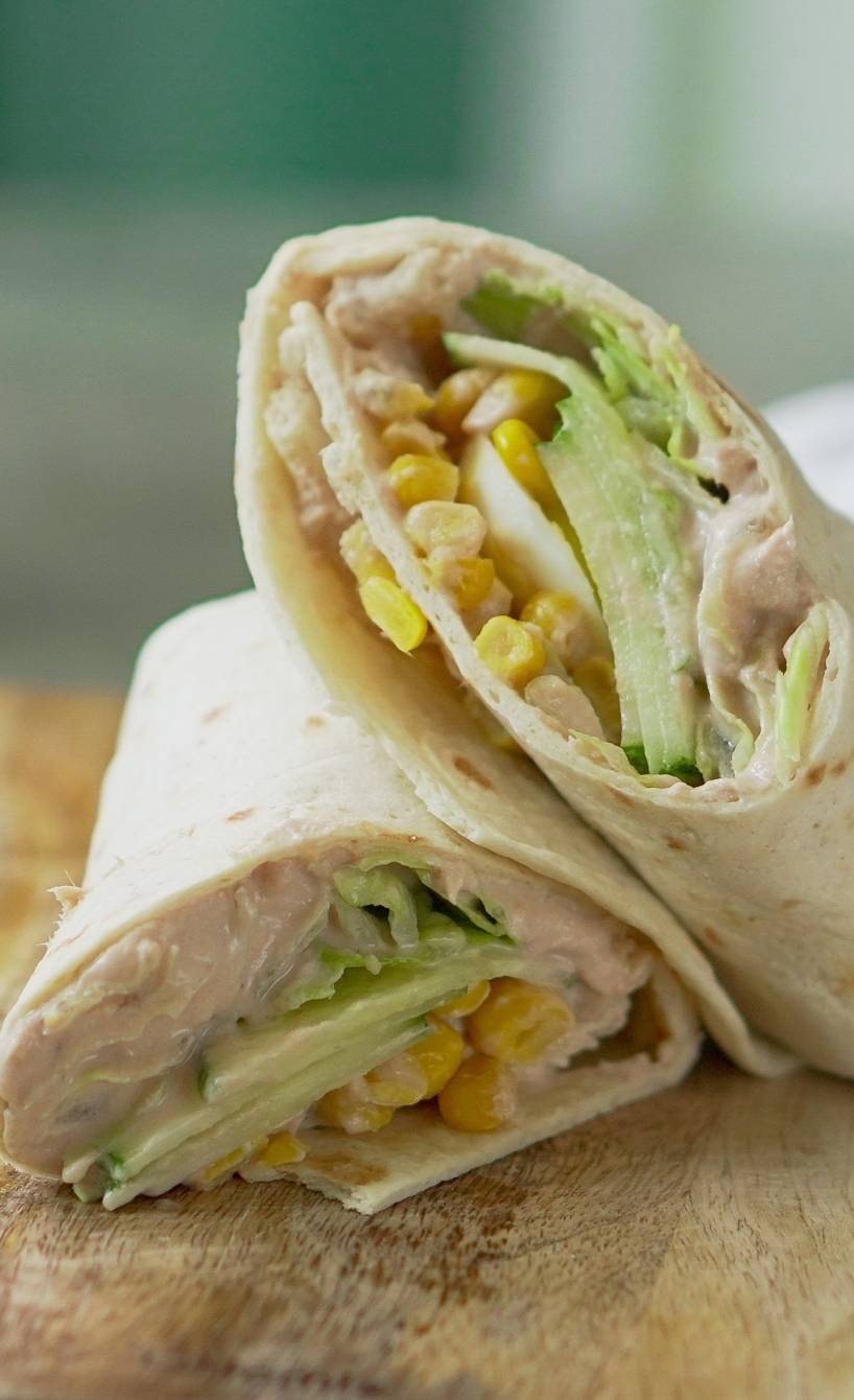Zwei Stücke eines halbierten „Tonnato-Style“ Wrap mit buntem Gemüse aufeinander liegend auf einem Holzbrett Zwei Stücke eines halbierten „Tonnato-Style“ Wrap mit buntem Gemüse aufeinander liegend auf einem Holzbrett