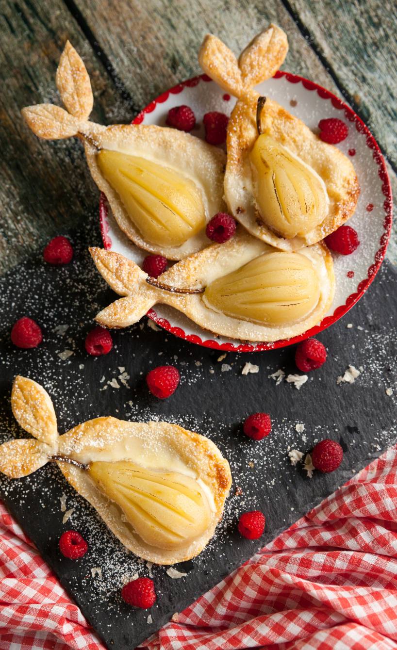 Vier selbstgebackene Birnen-Ricotta-Tartelettes aus Blätterteig geformt wie Birnen auf einer Servierplatte