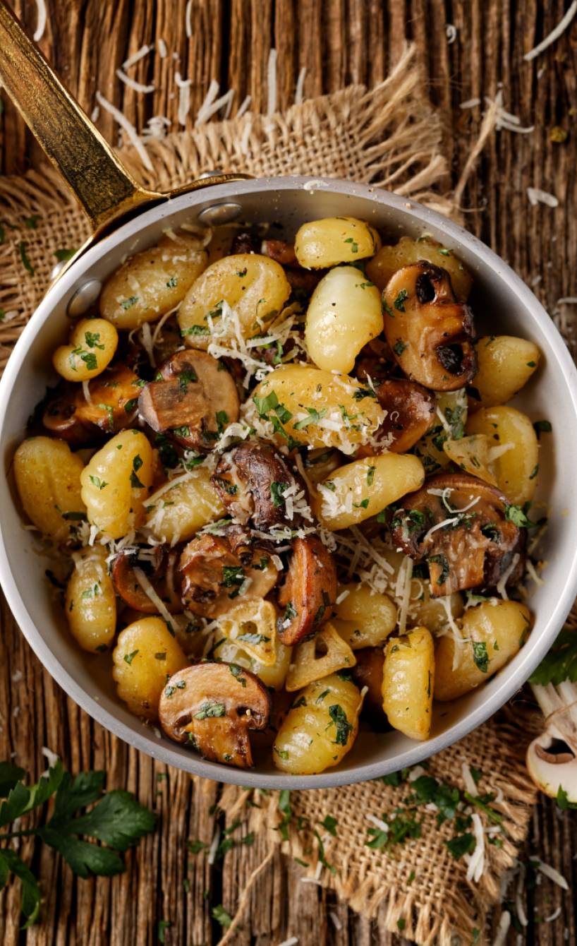 Pfanne mit gebratenen Champignons und Gnocchi in Knoblauchbutter getoppt von Parmesan auf eine Holztisch