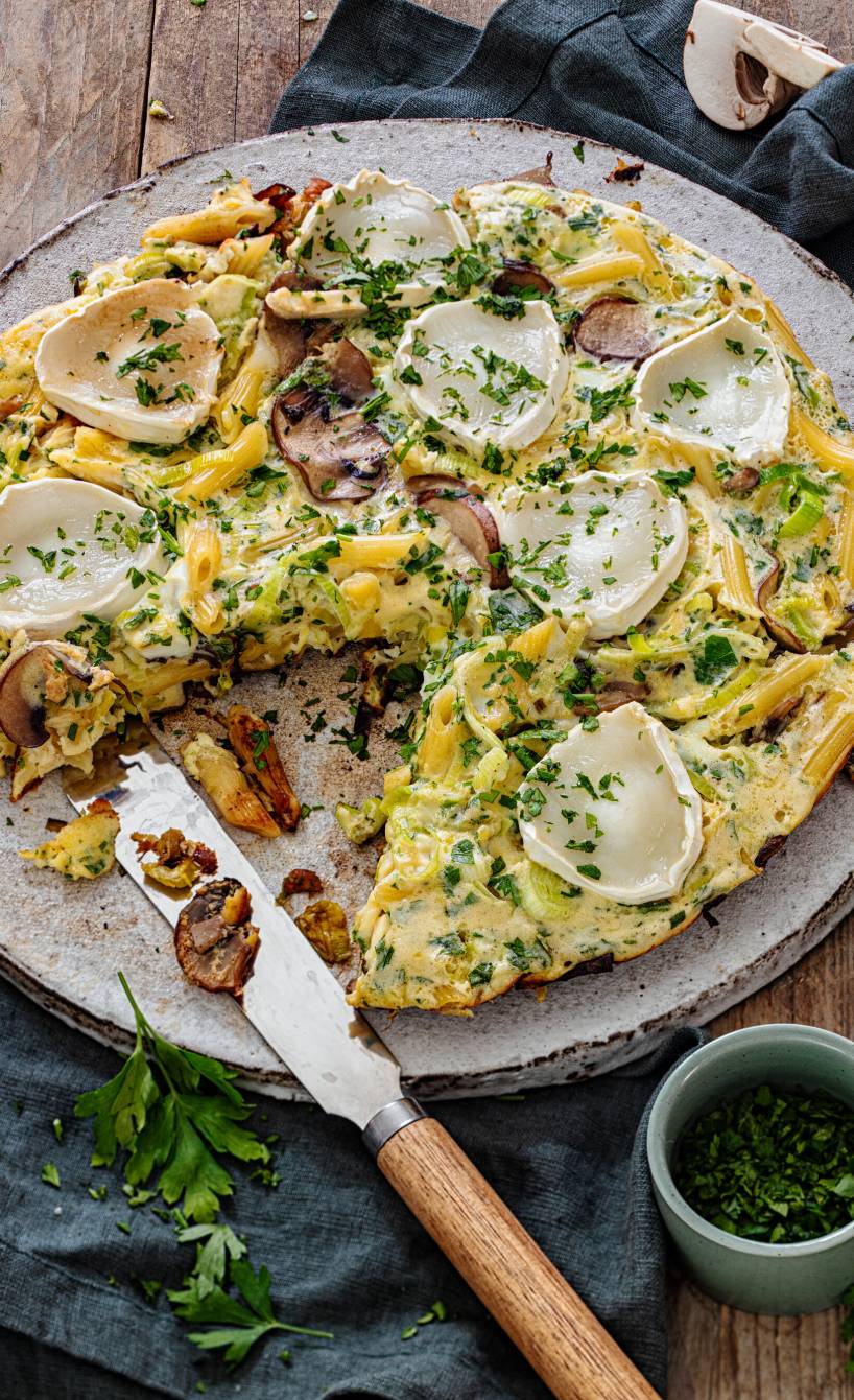 Nudel-Frittata mit Champignon und Lauch aus dem Ofen angerichtet auf einer Servierplatte getoppt von geschmolzenen Ziegenkäse-Scheiben