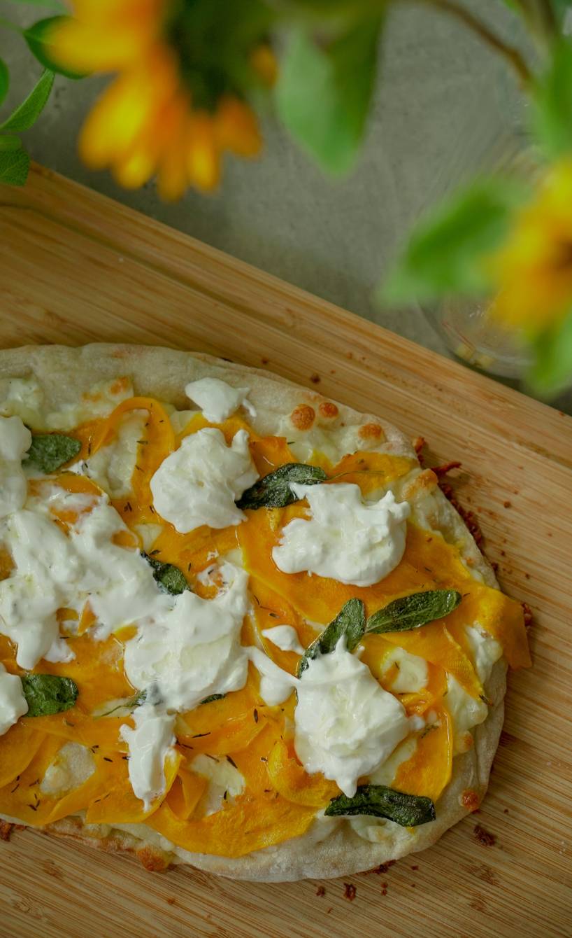 Gebackene ganze Pinsa belegt mit dünnen Kürbissalten und zerrupftem Burrata