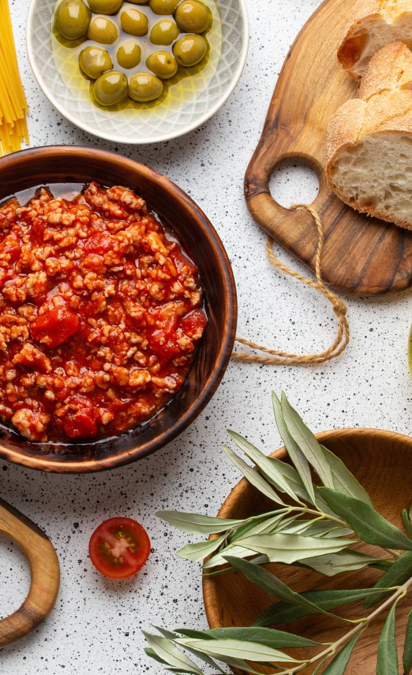 Selbstgekochte Bolognese auf einem Tisch mit Ciabatta und Oliven sowie Parmesan und Spaghetti