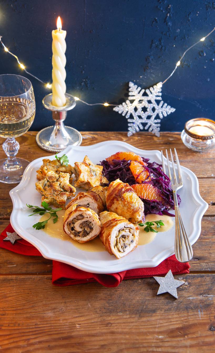 Hähncheninvoltini im Pancettamantel angerichtet mit gebratenem Serviettenknödel und Orangenrotkohl auf einem weihnachtlich dekorierten Tisch