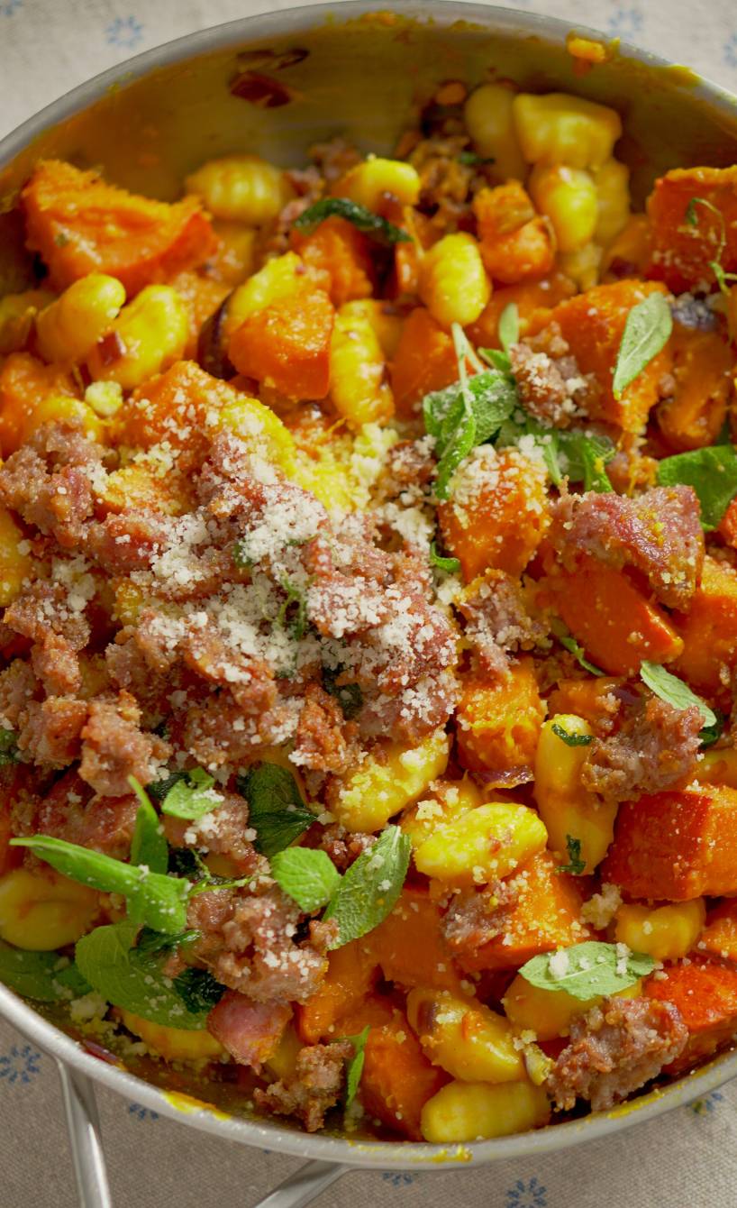 Hokkaido-Gnocchi-Pfanne mit Salsiccia angerichtet mit geriebenem Käse und Salbeiblättern auf einem Tisch