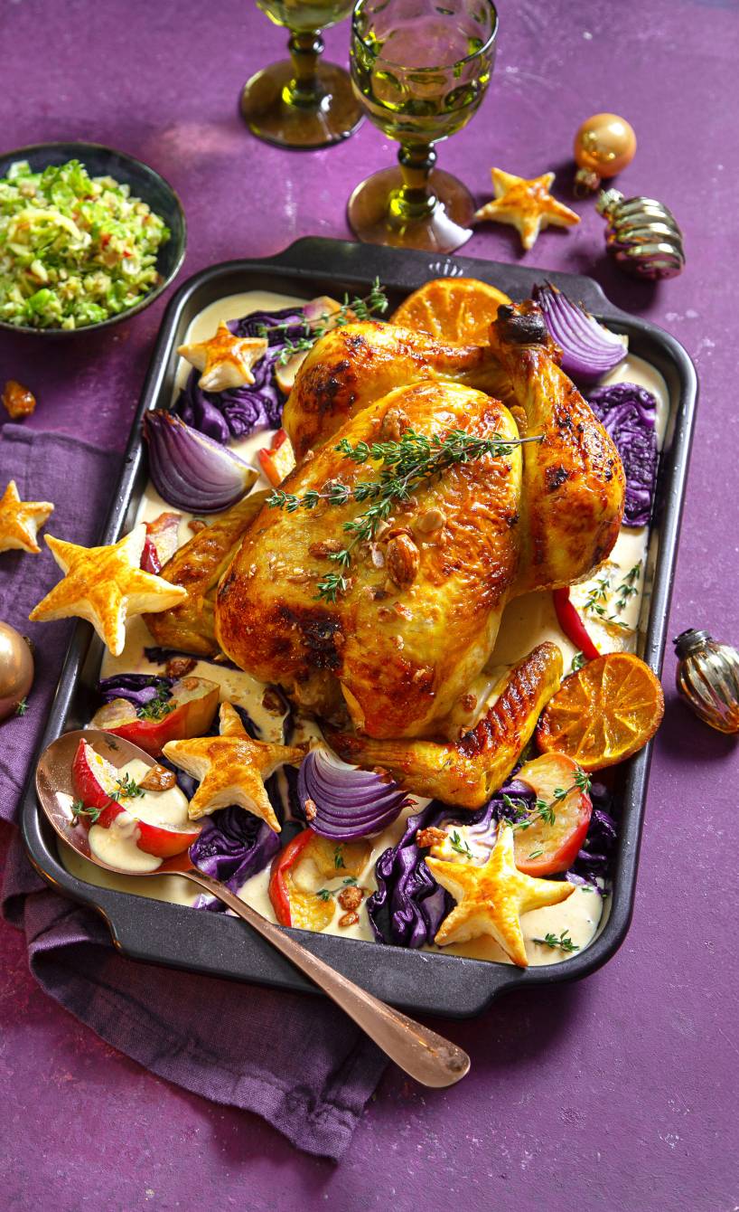 Gebackenes Orangen-Hähnchen auf Rotkohl in einer Auflaufform mit Soße getoppt von Blätterteigsternen auf einem weihnachtlich dekorierten Tisch