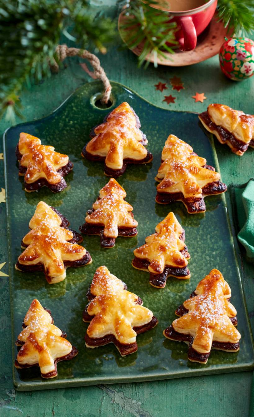 Selbstgebackene Nougat-Tannenbäume aus Blätterteig auf einem grünen Tonbrett auf einem weihnachtlich dekorierten Tisch