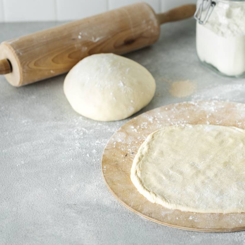 Pizzateig aus Semola ausgerollt auf einem Holzbrett
