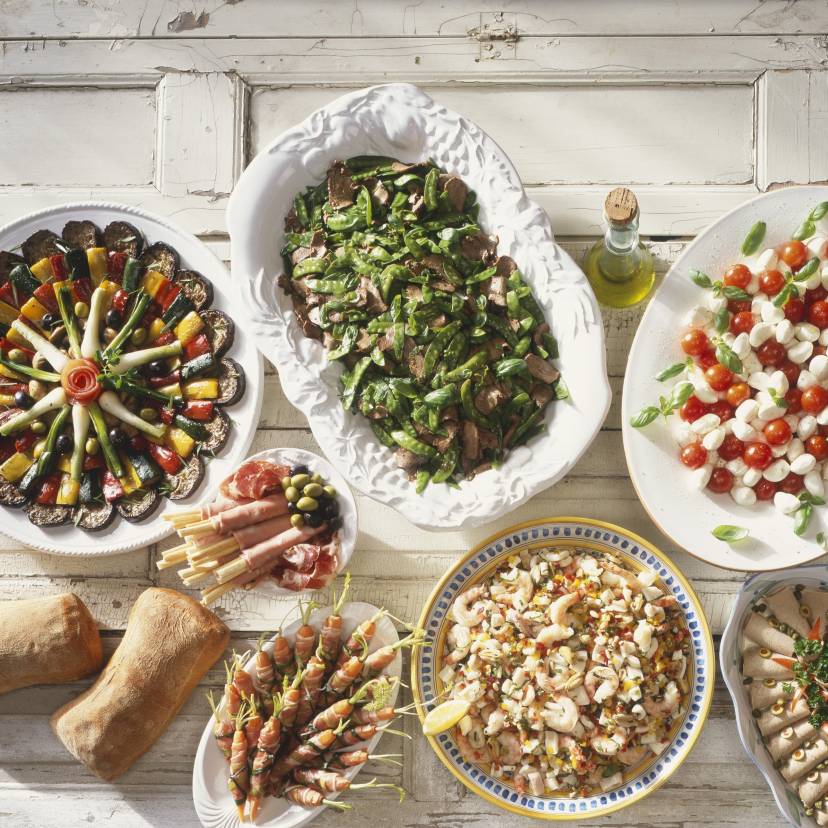 Italienisches Buffet aus Antipasti, Hauptgerichten und Desserts auf einem weißen Holztisch