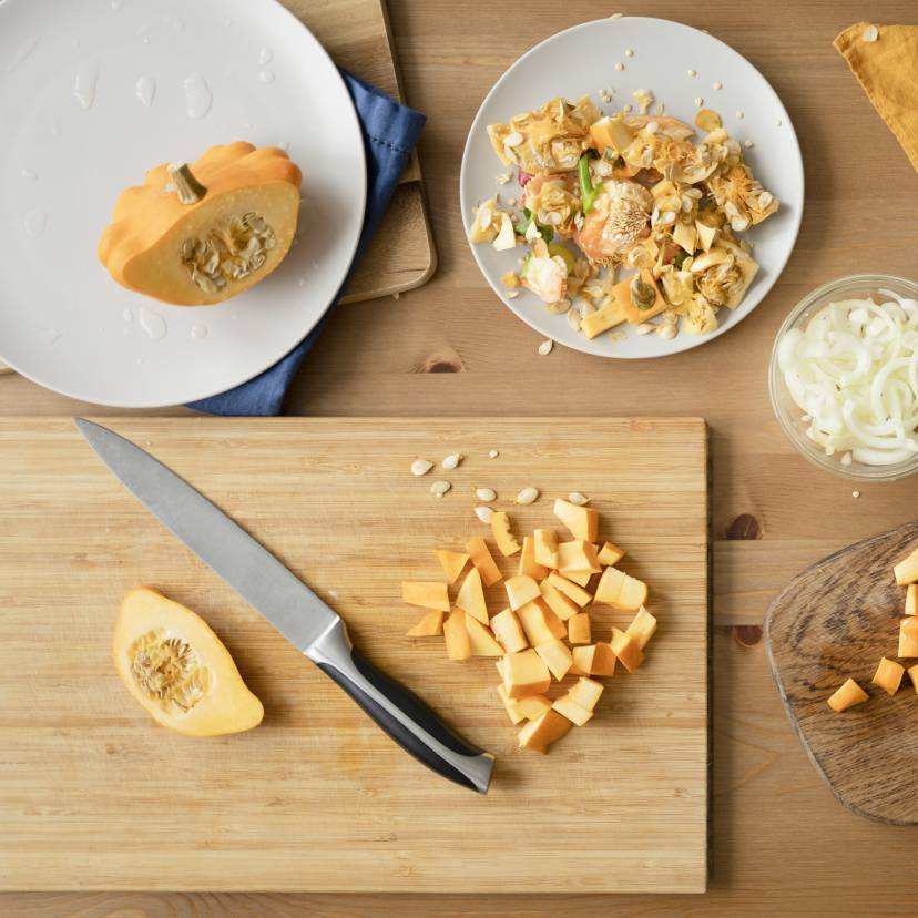 Kürbis nach italienischen Küchentipps in Würfel geschnitten auf einem Holztisch, daneben mehrere Herbstzutaten