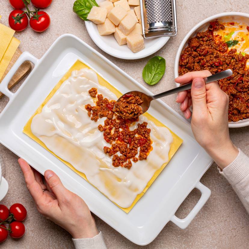 Blick von oben auf einen Tisch, auf dem gerade Lasagne zubereitet wird mit vielen Zutaten drumherum