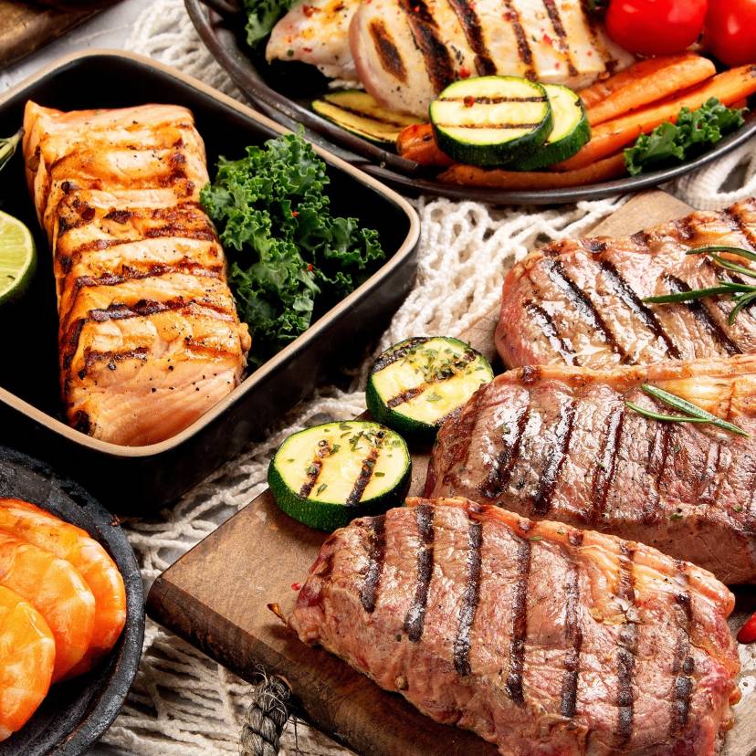 Esstisch mit Fleisch, Fisch, Brot und Gemüse vom Grill