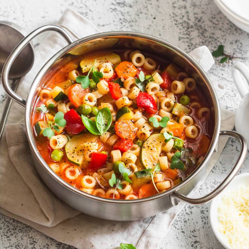 Selbstgekochte italienische Minestrone in einem Topf auf einem Tisch, daneben geröstete Ciabatta und Olivenöl