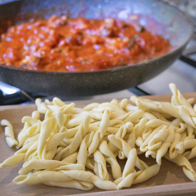 Selbstgemachte frische Nudeln auf einem Holzbrett, dahinter Tomatensoße in einer Pfanne