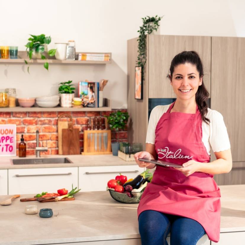 Serena Loddo sitzt auf der Kücheninsel in der So isst Italien Küche und sucht auf dem Tablet nach Rezepten für Ostern