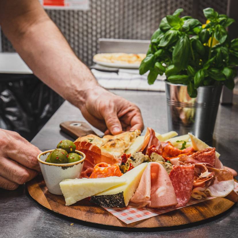 Ein Mann richtet verschiedene italienische Antipasti auf einem runden Holzbrett an
