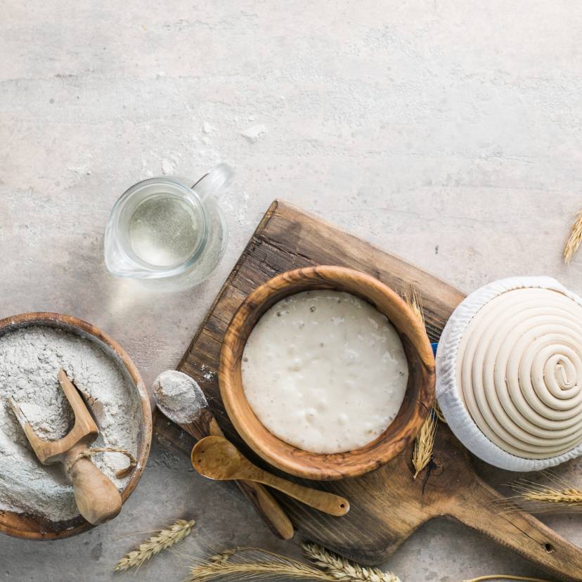 Aktiver Sauerteigstarter auf einem Tisch neben weiteren Brotbackzutaten wie Mehl und Wasser