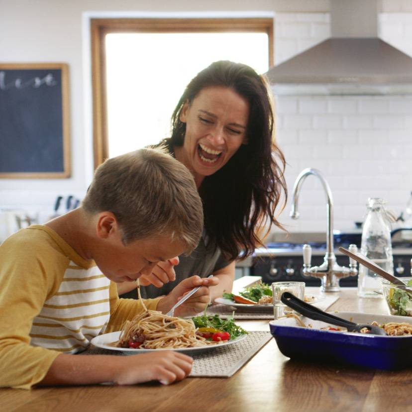 Eine vierköpfige Familie sitzt beim Abendessen an einer Kücheninsel und genießt Spaghetti